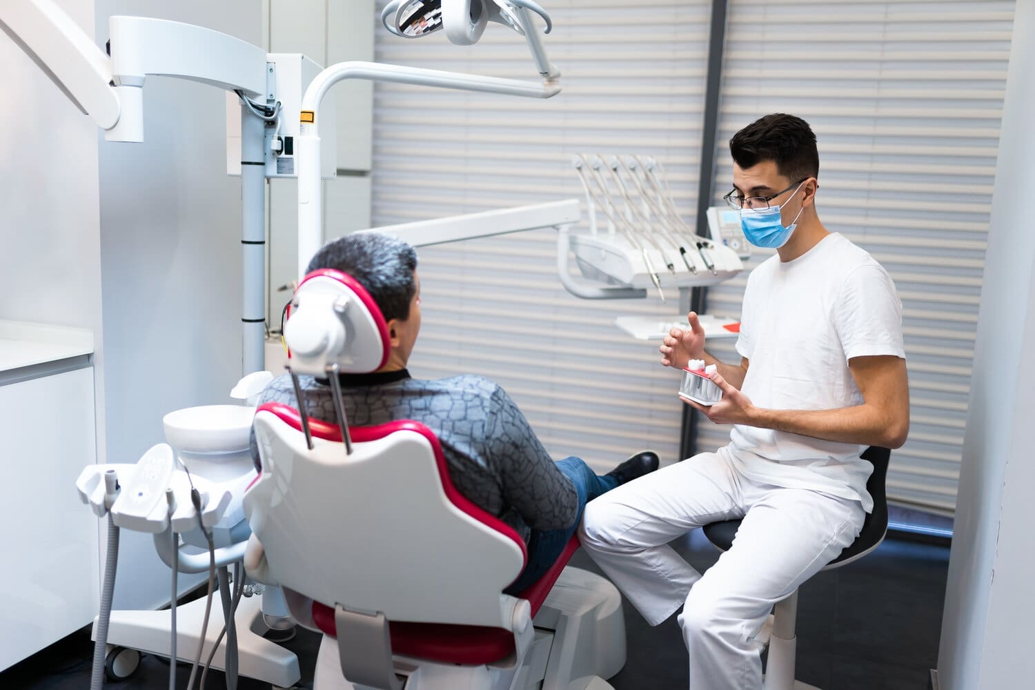 Dental surgeon with dental crown in hands model talks to patient about prosthetics. Man at the dentist's appointment